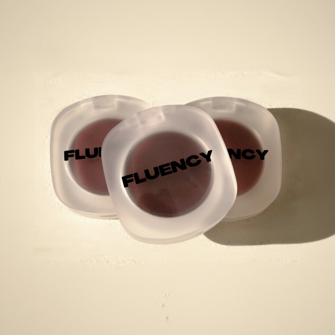 Two vegan blush makeup products in clear containers with 'Fluency' branding on a beige background
