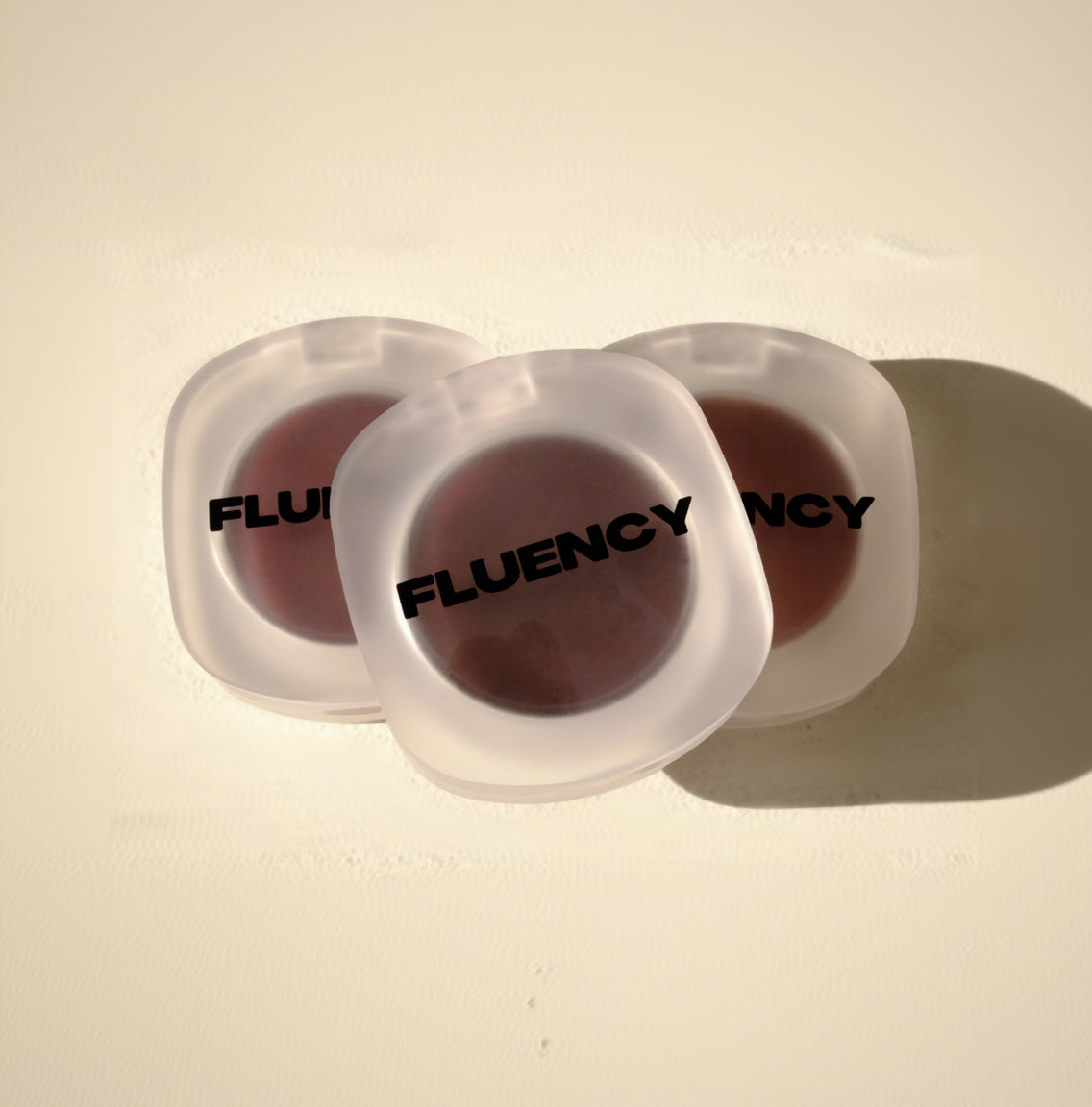 Two vegan blush makeup products in clear containers with 'Fluency' branding on a beige background