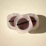 Two vegan blush makeup products in clear containers with 'Fluency' branding on a beige background