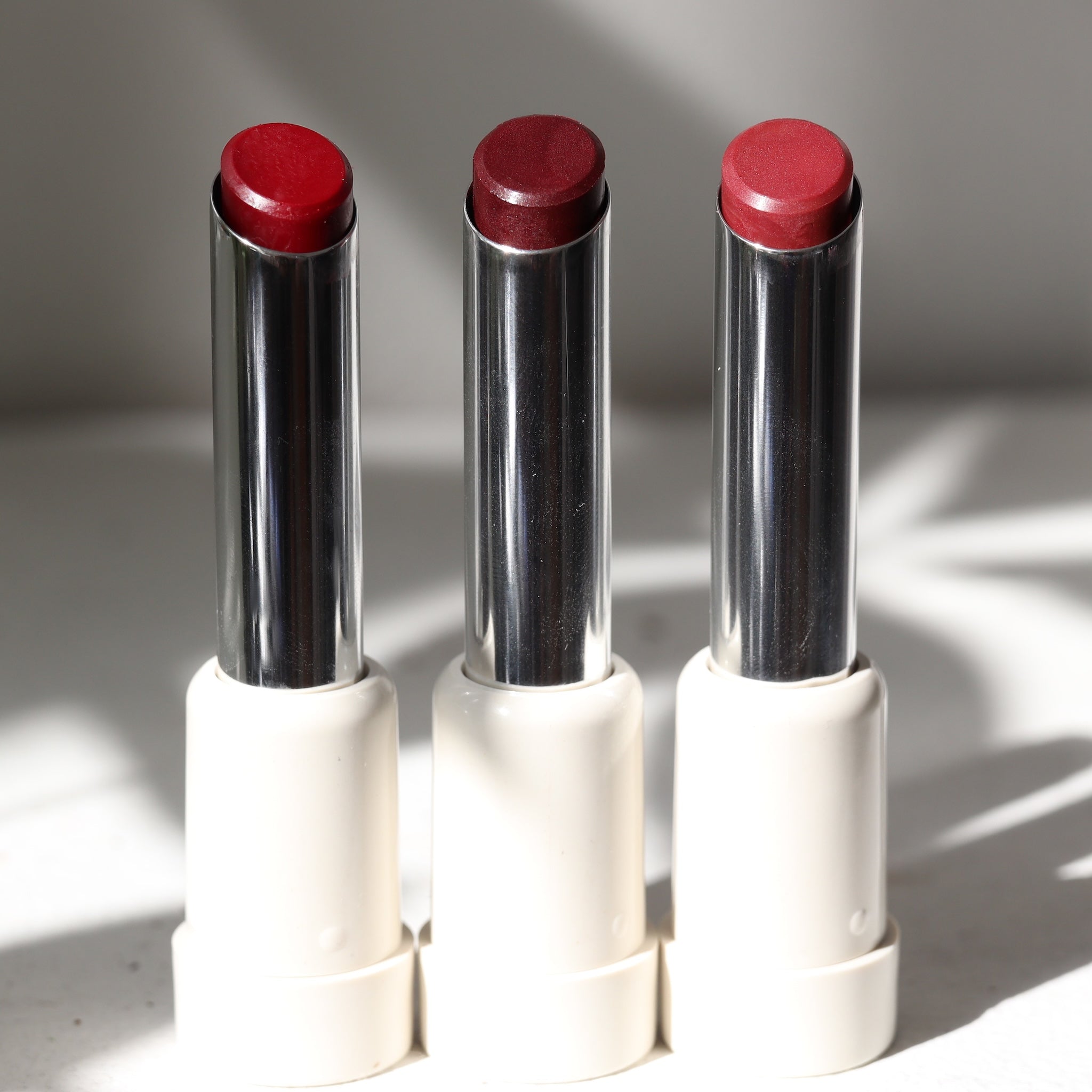 Three vegan lipsticks multisticks in red shades, each with a silver and white packaging, displayed side by side.