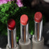three vegan, plant-based lipstick makeup colored from superfoods like beets, potatoes, radish, turmeric, and spirulina against a soft natural background with florals and nature.
