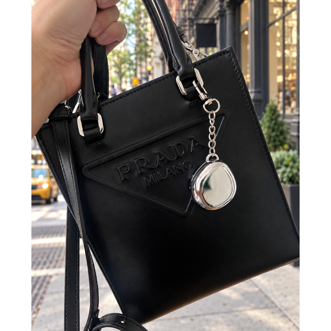 Fluency Color Me Ready silver chrome compact keychain attached to a black Prada bag on a New York City sidewalk
